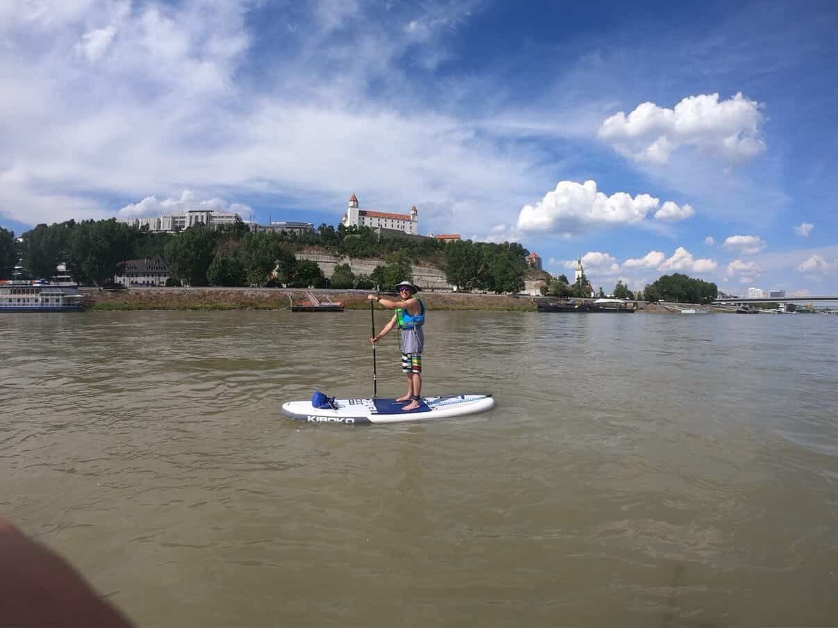Person paddle boarding on a river with a castle on a hilltop in the background