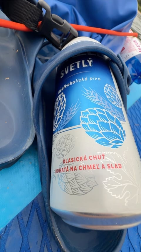 Svetly non-alcoholic beer can with blue and white label featuring hop designs, placed on a blue backpack