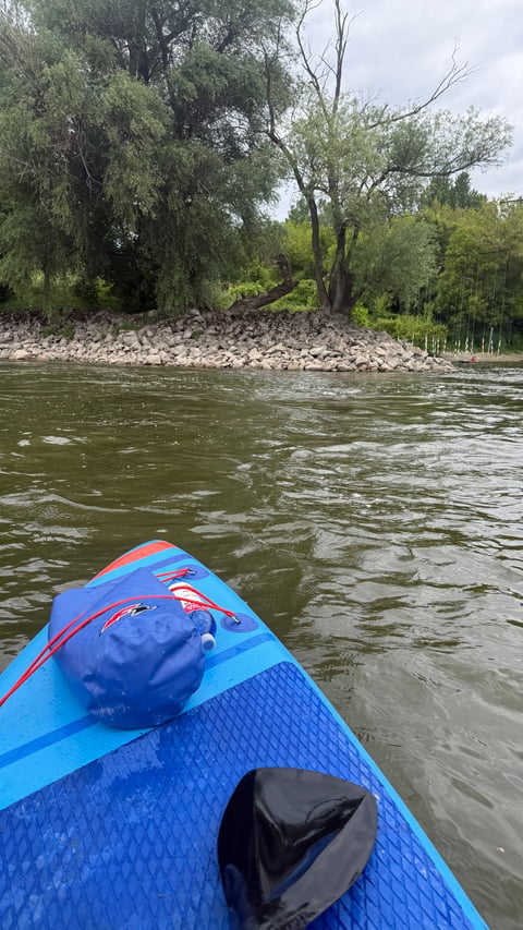 Blue paddleboard in river with stony bank and trees in background