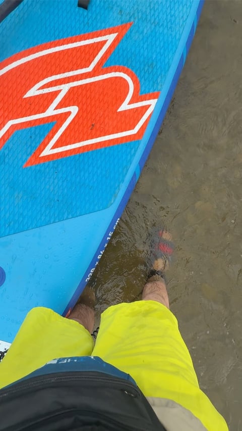 Person in bright yellow wetsuit wading into water next to blue surfboard with red graphic logo