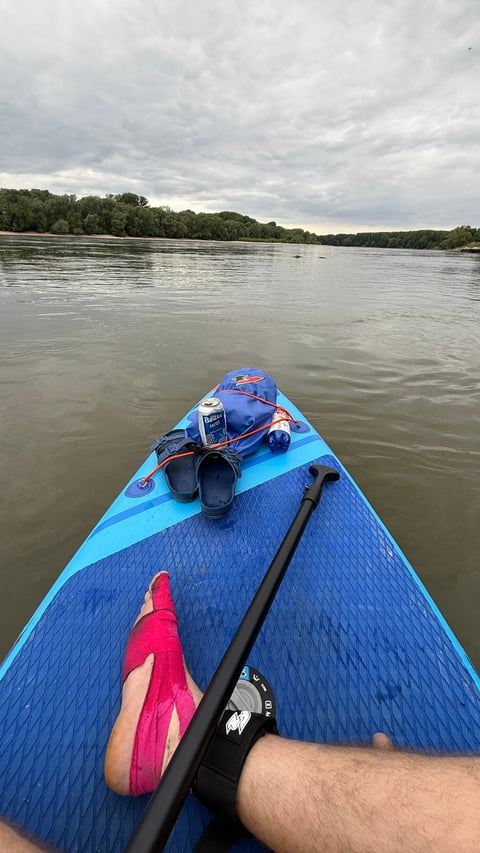 Person paddling a blue kayak on a wide river with forested banks and overcast sky