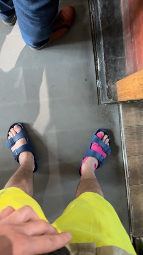 Person wearing bright neon yellow pants and blue sandals standing on a light gray floor next to darker flooring